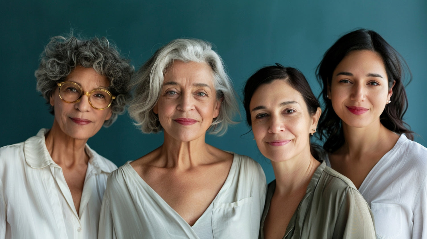 A group portrait of four women of different ages, all smiling confidently against a teal background. They represent diverse stages of ageing with graceful skin and natural beauty.